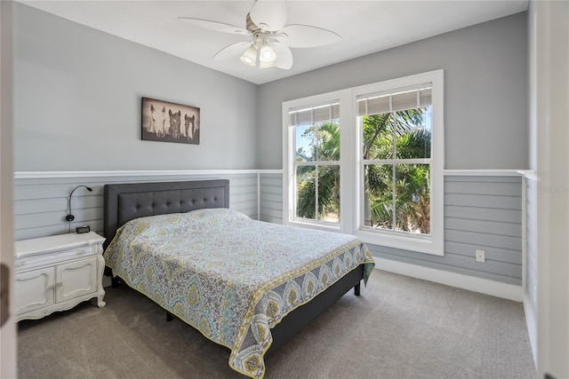 bedroom with wainscoting, dark carpet, and a ceiling fan