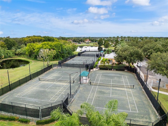 view of tennis court with a water view and fence