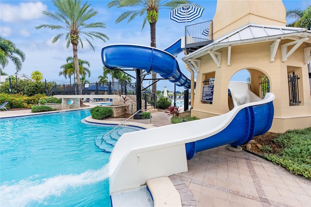 community pool with a patio area, a water slide, and fence