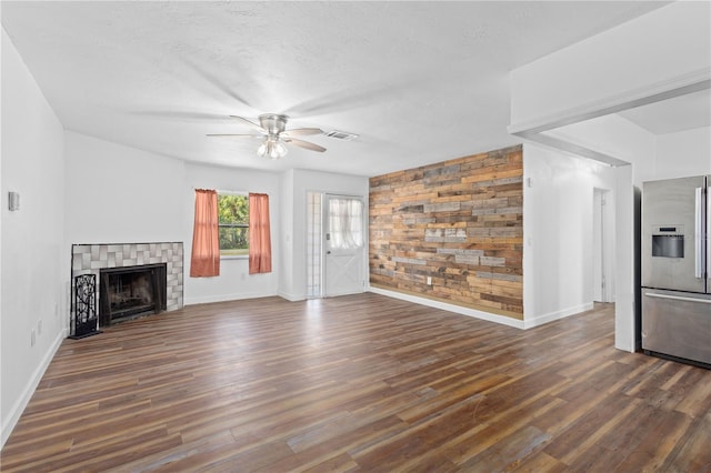 unfurnished living room with wooden walls, an accent wall, a fireplace, visible vents, and dark wood finished floors