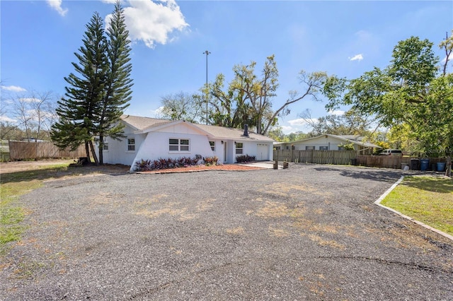 ranch-style home with gravel driveway and fence