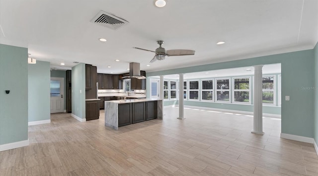 kitchen with island exhaust hood, decorative columns, visible vents, open floor plan, and dark brown cabinetry