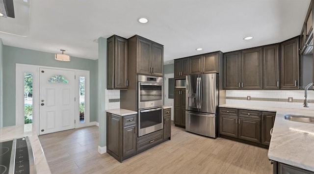 kitchen featuring stainless steel appliances, light wood-style floors, dark brown cabinetry, and decorative backsplash