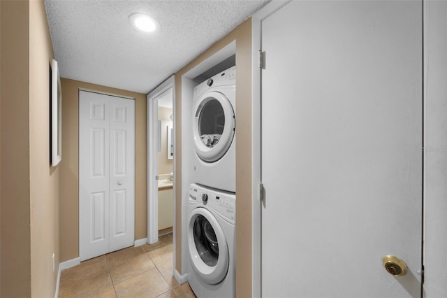 laundry area with a textured ceiling, light tile patterned floors, laundry area, stacked washer / dryer, and baseboards