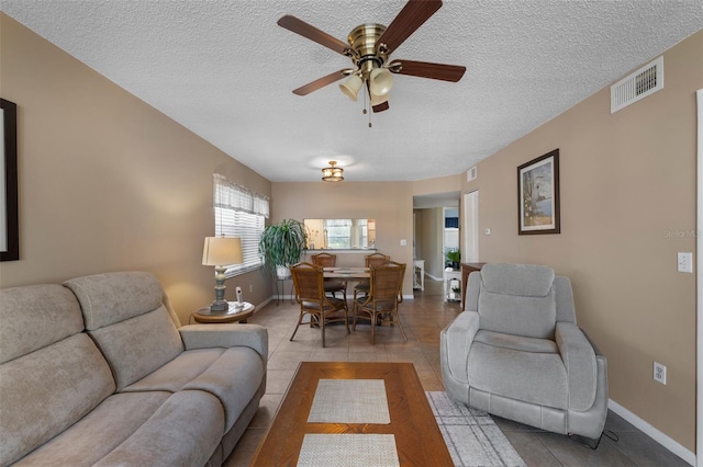 tiled living room with a textured ceiling, ceiling fan, visible vents, and baseboards