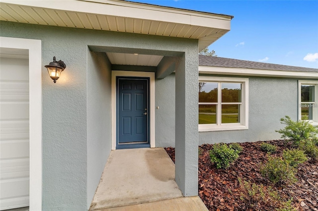 entrance to property with roof with shingles, an attached garage, and stucco siding