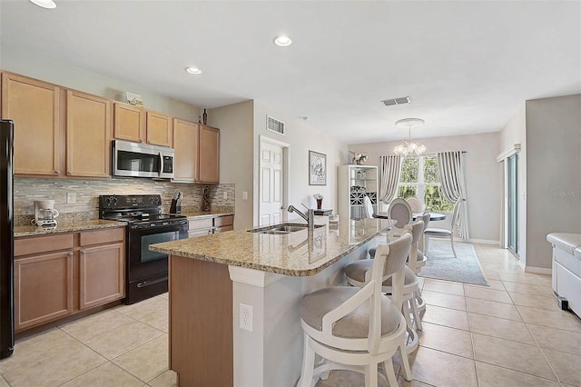 kitchen with light tile patterned floors, decorative backsplash, light stone countertops, black appliances, and a sink