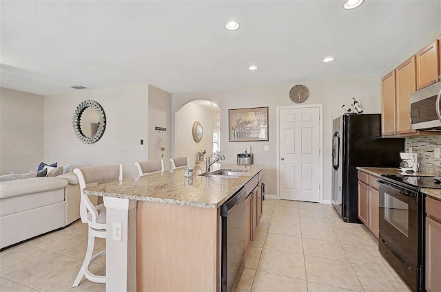 kitchen featuring light tile patterned floors, black appliances, a kitchen bar, and a sink