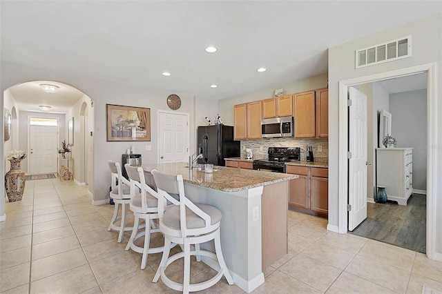 kitchen with arched walkways, light tile patterned floors, a breakfast bar area, visible vents, and black appliances