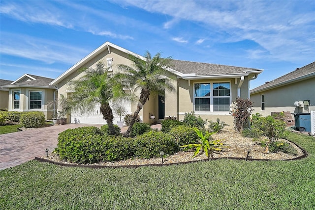 view of front of home with a front lawn, decorative driveway, an attached garage, and stucco siding