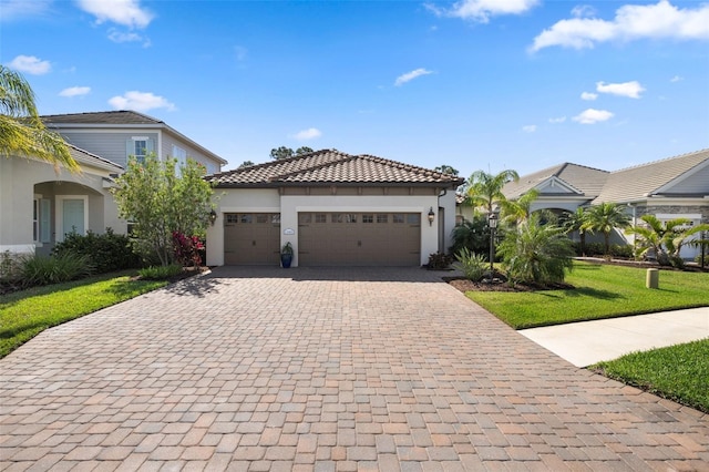 mediterranean / spanish house with an attached garage, a tile roof, decorative driveway, stucco siding, and a front lawn