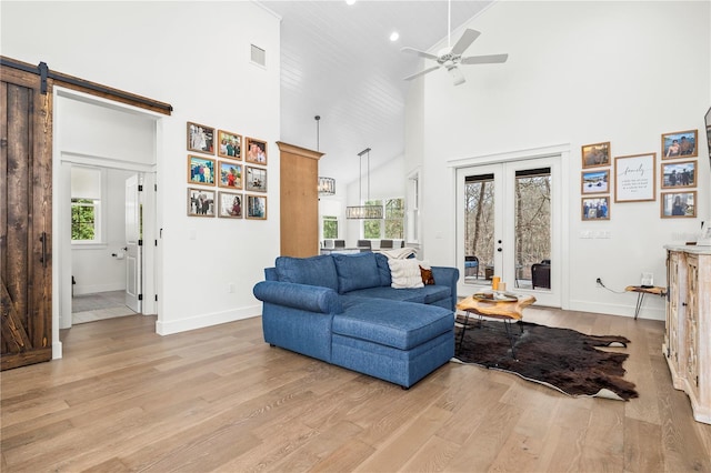 living room with french doors, visible vents, a barn door, light wood-style floors, and high vaulted ceiling