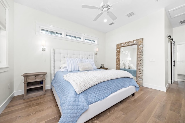 bedroom with a barn door, wood finished floors, visible vents, and baseboards