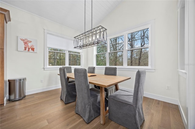 dining room with lofted ceiling, baseboards, a notable chandelier, and light wood finished floors