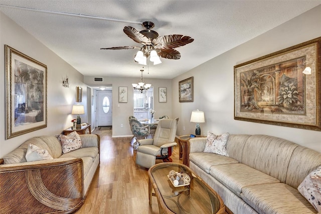 living room featuring visible vents, baseboards, wood finished floors, a textured ceiling, and ceiling fan with notable chandelier