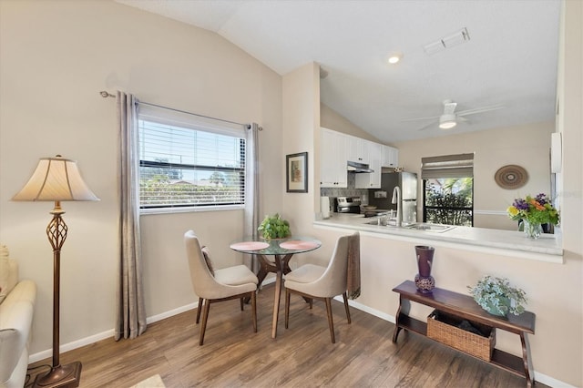 dining area with visible vents, baseboards, ceiling fan, vaulted ceiling, and light wood-type flooring