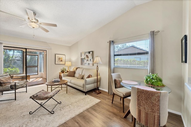 living area featuring a ceiling fan, lofted ceiling, baseboards, and wood finished floors