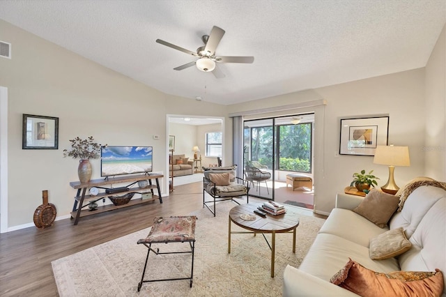 living room featuring a textured ceiling, ceiling fan, wood finished floors, baseboards, and vaulted ceiling