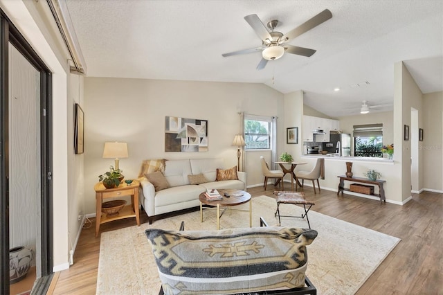 living room with baseboards, ceiling fan, vaulted ceiling, a textured ceiling, and light wood-type flooring