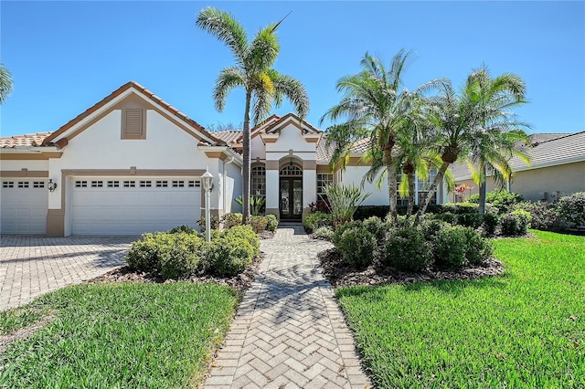 mediterranean / spanish-style house featuring stucco siding, a tile roof, decorative driveway, a front yard, and a garage