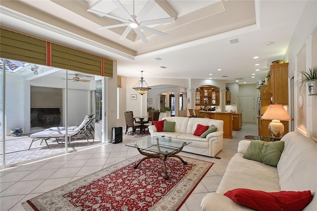 living room with light tile patterned floors, a ceiling fan, decorative columns, arched walkways, and a raised ceiling