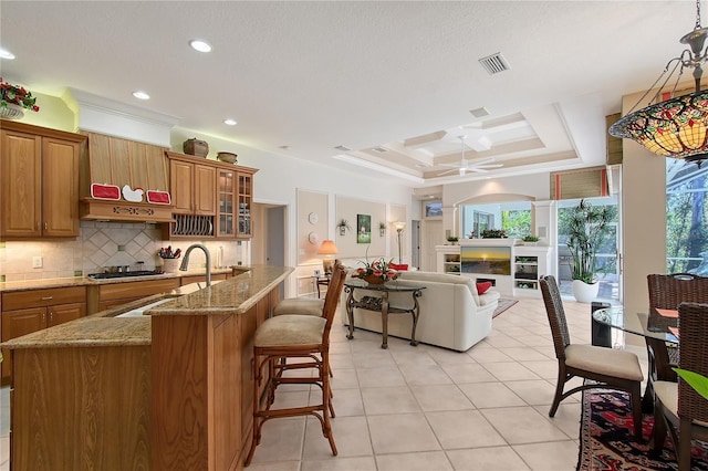 kitchen with backsplash, a tray ceiling, brown cabinets, a fireplace, and a sink