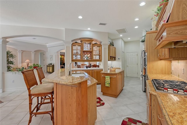 kitchen featuring a breakfast bar, an island with sink, a sink, light stone countertops, and stainless steel gas cooktop