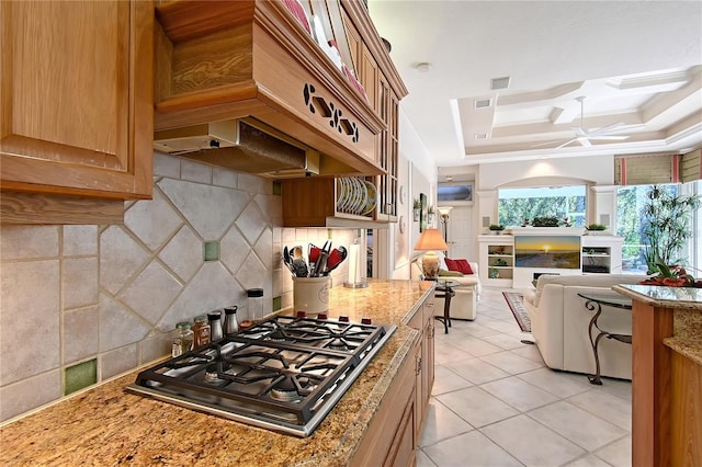 kitchen featuring custom range hood, a tray ceiling, a fireplace, decorative backsplash, and stainless steel gas cooktop