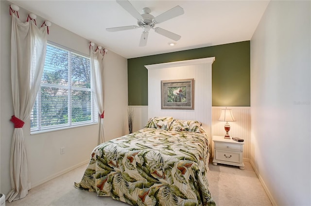 bedroom featuring baseboards, light colored carpet, a wainscoted wall, and ceiling fan