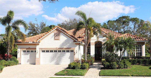 mediterranean / spanish home with stucco siding, a tile roof, decorative driveway, and a garage