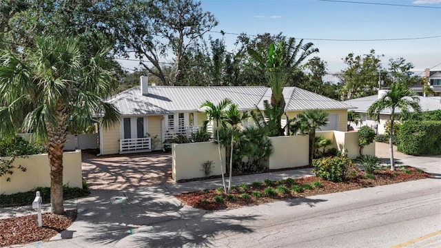 view of front of property featuring driveway, a fenced front yard, a chimney, and metal roof
