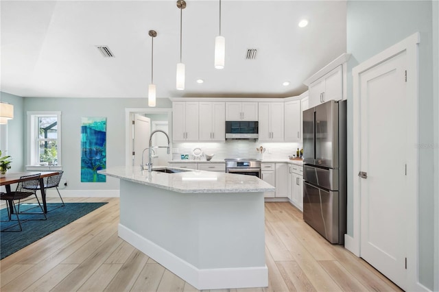 kitchen with a sink, white cabinets, freestanding refrigerator, an island with sink, and pendant lighting