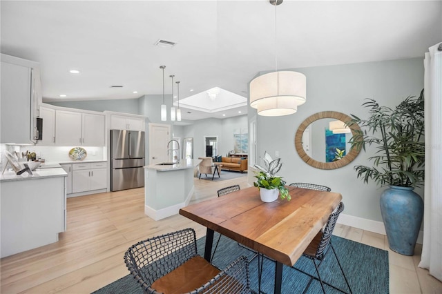 dining space featuring light wood finished floors, recessed lighting, visible vents, vaulted ceiling with skylight, and baseboards