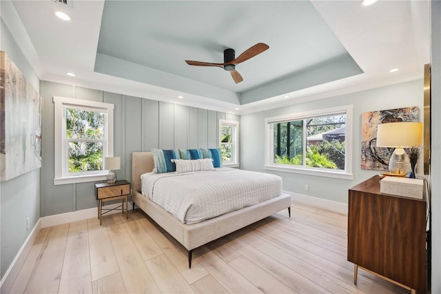 bedroom with light wood finished floors, baseboards, multiple windows, and a tray ceiling