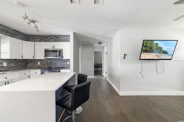 kitchen with dark wood-type flooring, white cabinets, appliances with stainless steel finishes, tasteful backsplash, and a kitchen bar