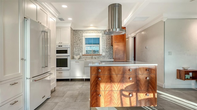 kitchen with tasteful backsplash, high end fridge, white cabinets, island range hood, and black electric cooktop