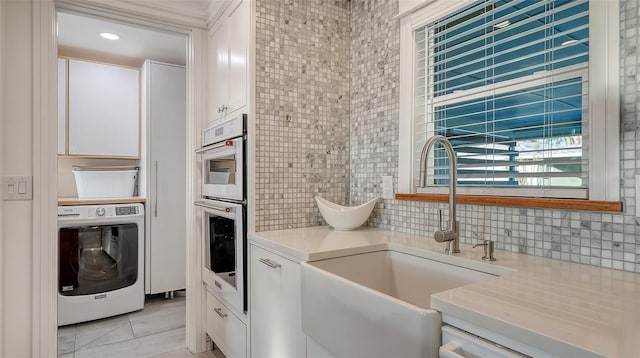 kitchen with washer / clothes dryer, white cabinets, a sink, and light countertops