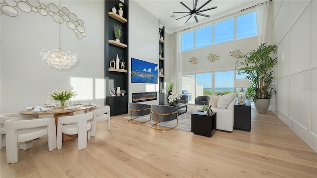 living area with a towering ceiling, light wood finished floors, a decorative wall, and a glass covered fireplace