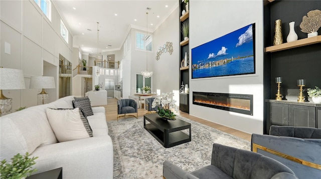living area with wood finished floors, a towering ceiling, a glass covered fireplace, built in shelves, and recessed lighting