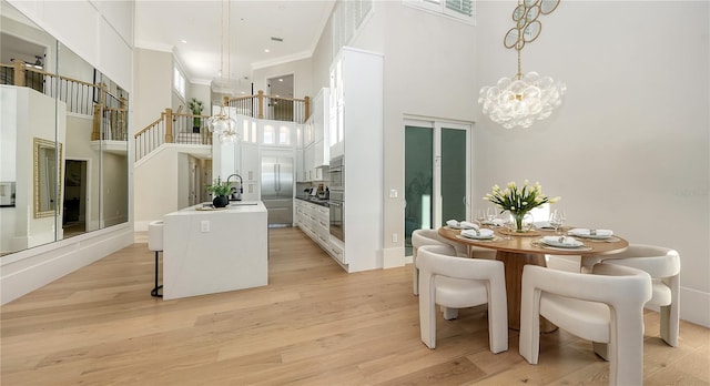 dining space with a chandelier, a towering ceiling, ornamental molding, and light wood-type flooring