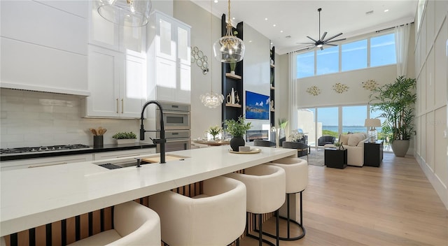 kitchen with a high ceiling, gas cooktop, a sink, white cabinets, and decorative backsplash