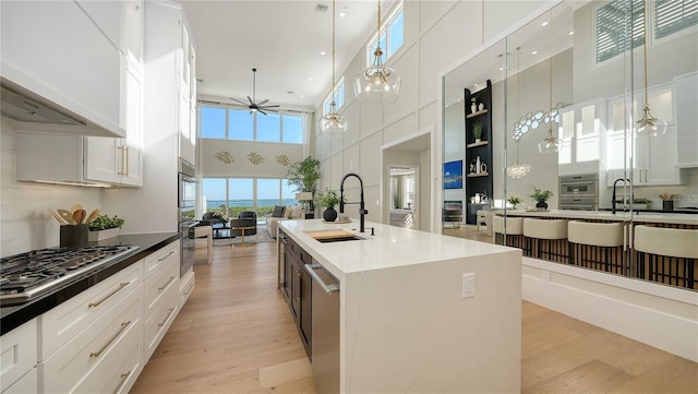 kitchen featuring a towering ceiling, a sink, a ceiling fan, light wood-type flooring, and hanging light fixtures