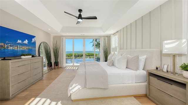 bedroom with a raised ceiling, access to exterior, light wood-style floors, and a ceiling fan