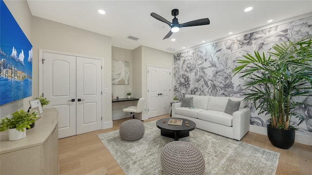 living area with ceiling fan, light wood-type flooring, an accent wall, and recessed lighting