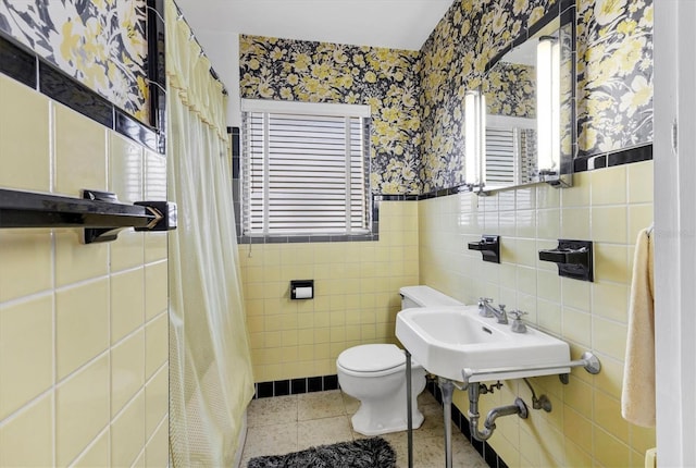 bathroom featuring wallpapered walls, toilet, a wainscoted wall, tile patterned flooring, and tile walls