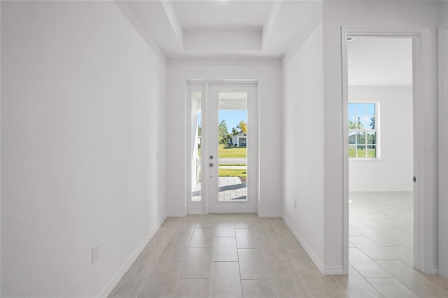 foyer entrance featuring a tray ceiling and baseboards