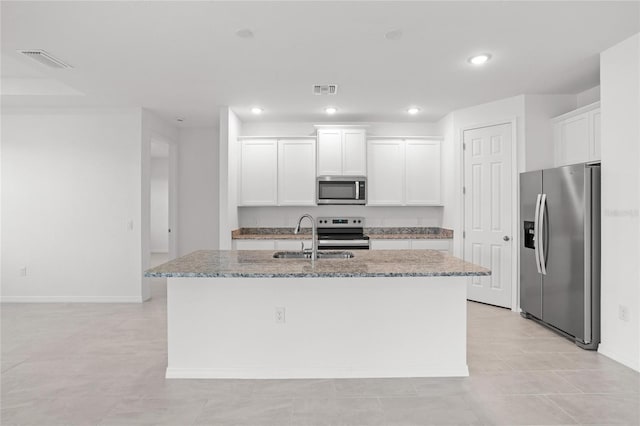 kitchen featuring a center island with sink, light stone counters, stainless steel appliances, white cabinetry, and a sink