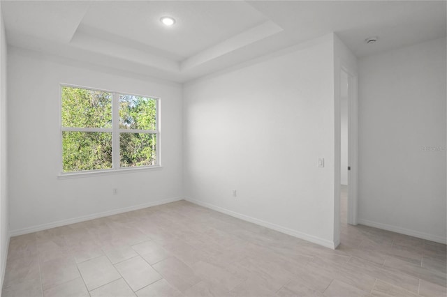 empty room featuring a tray ceiling, baseboards, and light tile patterned floors