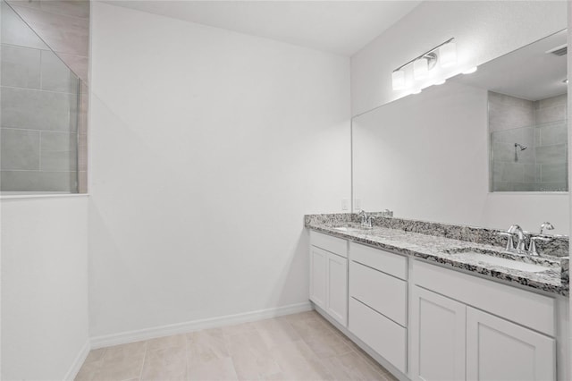 full bathroom featuring double vanity, baseboards, a sink, and tiled shower