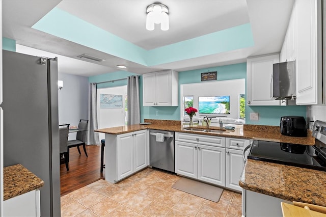 kitchen with white cabinets, dark stone counters, appliances with stainless steel finishes, a peninsula, and a sink